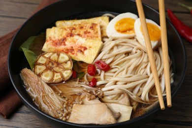 Photo of Tasty ramen with enoki and king oyster (eryngii) mushrooms in bowl on table, closeup
