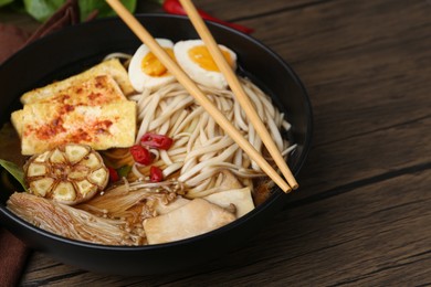 Photo of Tasty ramen with enoki and king oyster (eryngii) mushrooms in bowl on wooden table, closeup