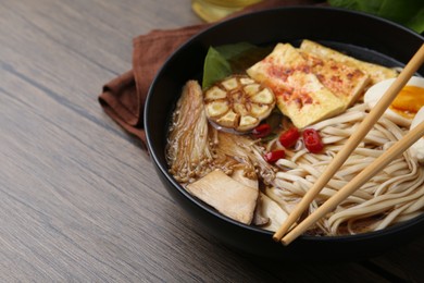 Photo of Tasty ramen with enoki and king oyster (eryngii) mushrooms in bowl on wooden table, closeup