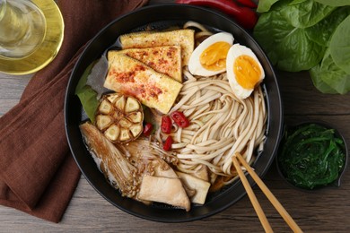 Photo of Tasty ramen with enoki and king oyster (eryngii) mushrooms in bowl on wooden table, flat lay