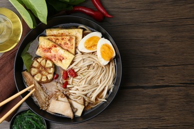 Photo of Tasty ramen with enoki and king oyster (eryngii) mushrooms in bowl on wooden table, top view. Space for text