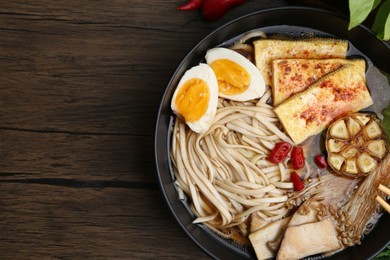 Photo of Tasty ramen with enoki and king oyster (eryngii) mushrooms in bowl on wooden table, top view. Space for text