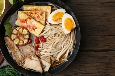 Photo of Tasty ramen with enoki and king oyster (eryngii) mushrooms in bowl on wooden table, top view