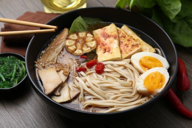 Photo of Tasty ramen with enoki and king oyster (eryngii) mushrooms in bowl on wooden table, closeup