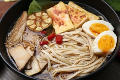 Photo of Tasty ramen with enoki and king oyster (eryngii) mushrooms in bowl on table, closeup