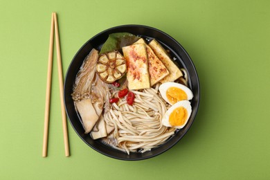 Photo of Tasty ramen with enoki and king oyster (eryngii) mushrooms in bowl on green table, flat lay