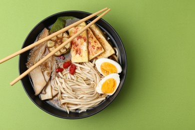 Photo of Tasty ramen with enoki and king oyster (eryngii) mushrooms in bowl on green table, top view