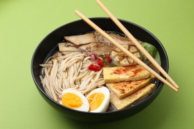 Photo of Tasty ramen with enoki and king oyster (eryngii) mushrooms in bowl on green table, closeup