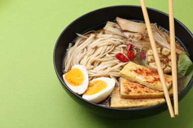Photo of Tasty ramen with enoki and king oyster (eryngii) mushrooms in bowl on green table, closeup