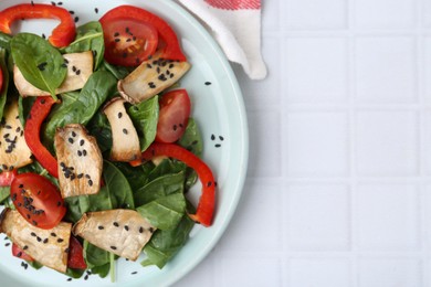 Photo of Tasty salad with eryngium mushrooms, vegetables, spinach and sesame on white tiled table, top view. Space for text