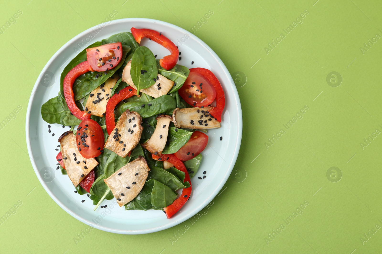 Tasty salad with eryngium mushrooms, vegetables, spinach and sesame on green background, top view. Space for text Photo of Tasty salad with eryngium mushrooms, vegetables, spinach and sesame on green background, top view. Space for text
