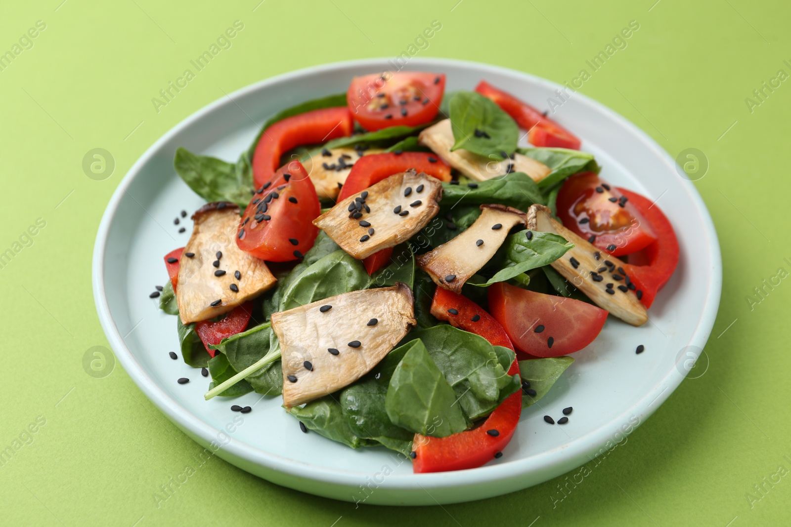 Tasty salad with eryngium mushrooms, vegetables, spinach and sesame on green background, closeup Photo of Tasty salad with eryngium mushrooms, vegetables, spinach and sesame on green background, closeup