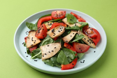 Photo of Tasty salad with eryngium mushrooms, vegetables, spinach and sesame on green background, closeup