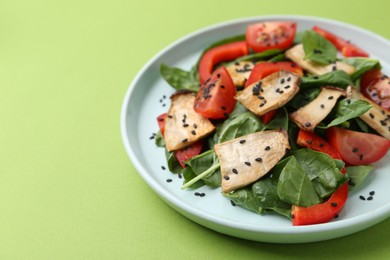 Photo of Tasty salad with eryngium mushrooms, vegetables, spinach and sesame on green background, closeup. Space for text