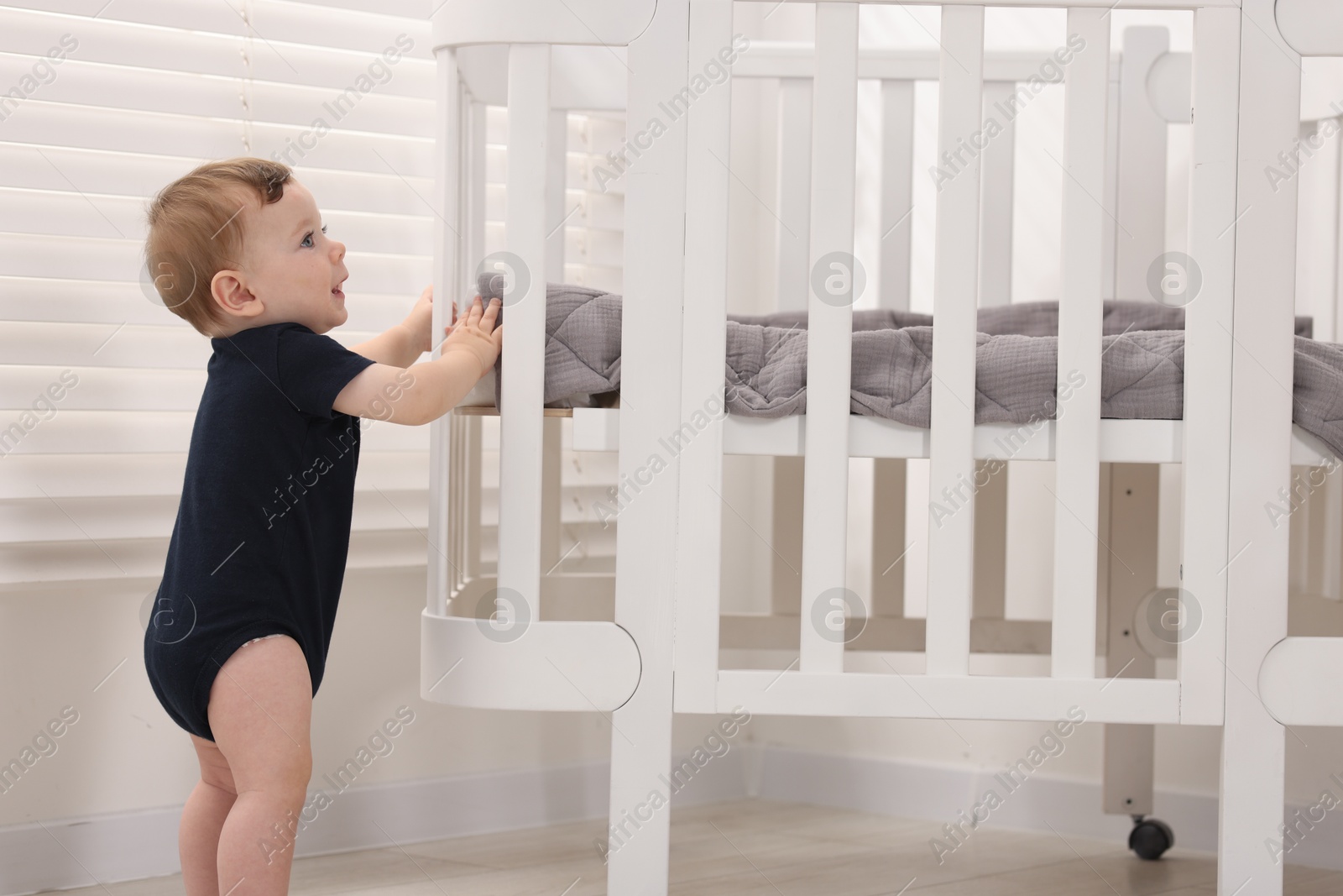Photo of Cute little baby near crib at home