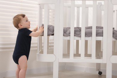 Photo of Cute little baby near crib at home