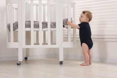 Photo of Cute little baby near crib at home