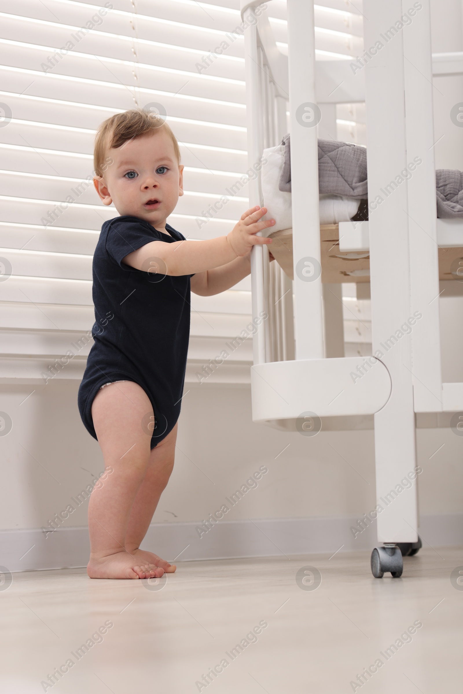Photo of Cute little baby near crib at home