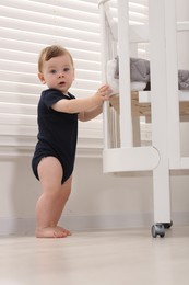 Photo of Cute little baby near crib at home