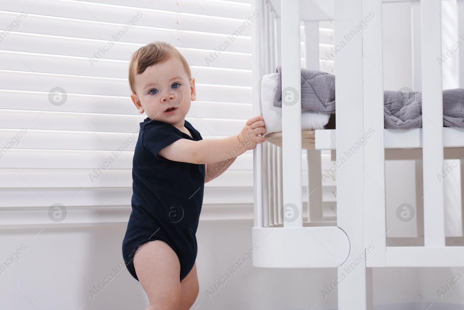 Photo of Cute little baby near crib at home