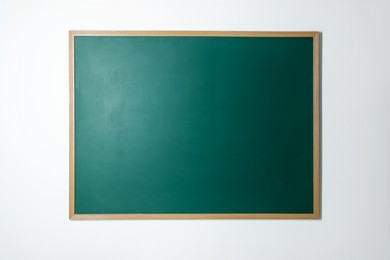 Photo of Blank green chalkboard on white wall indoors