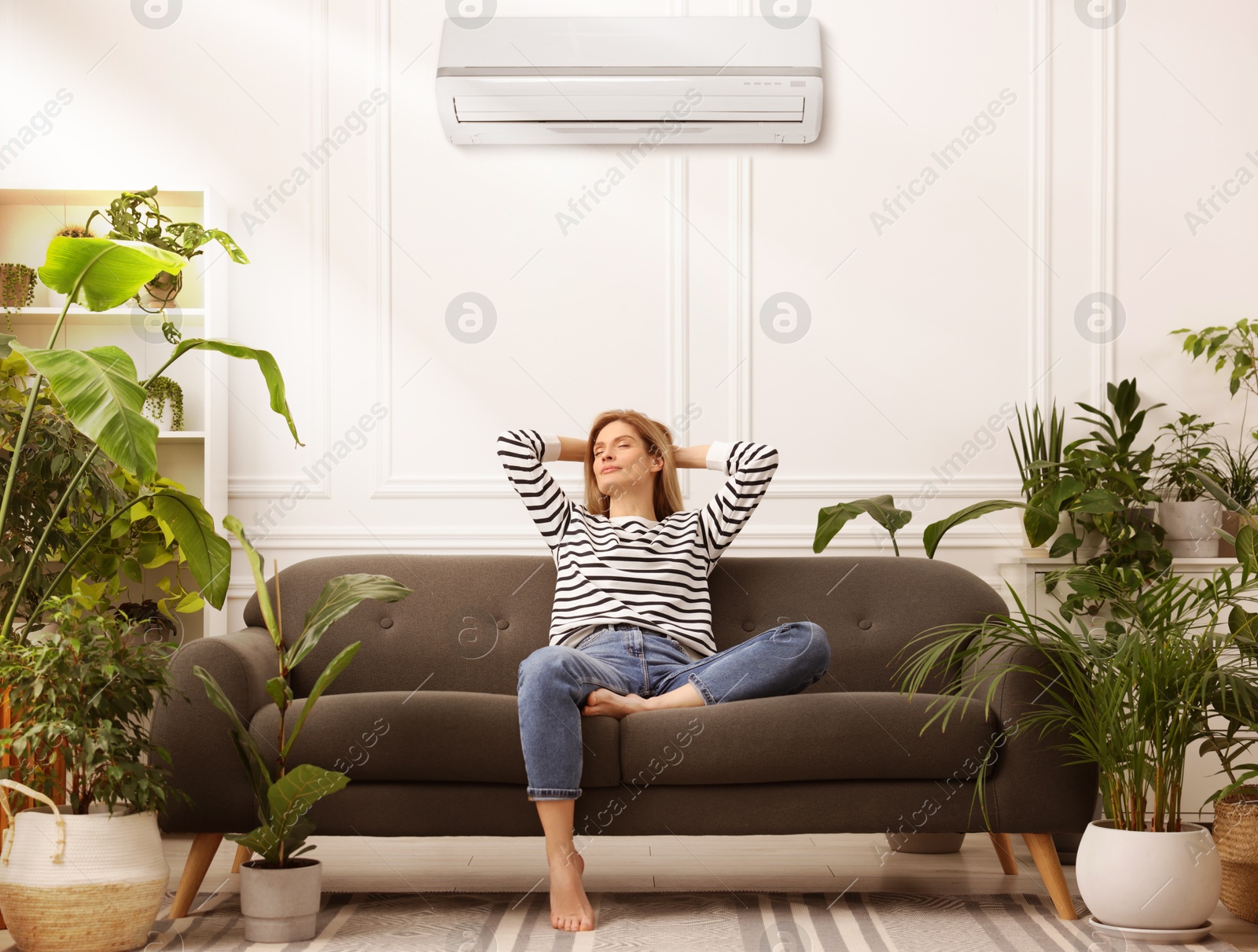 Woman relaxing on sofa surrounded by potted houseplants at home. Air conditioner keeping comfortable temperature in room Image of Woman relaxing on sofa surrounded by potted houseplants at home. Air conditioner keeping comfortable temperature in room
