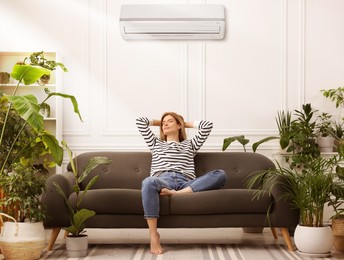 Image of Woman relaxing on sofa surrounded by potted houseplants at home. Air conditioner keeping comfortable temperature in room
