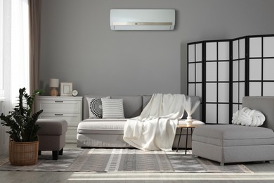 Image of Sofa with blanket and folding screen in room. Air conditioner keeping comfortable temperature indoors