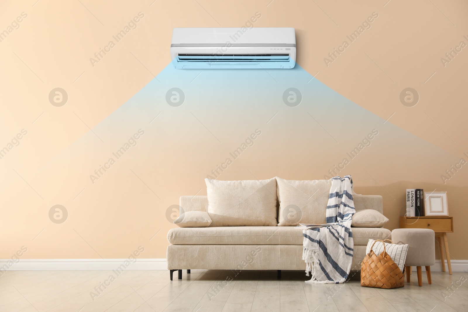 Image of Sofa with pillows, blanket, pouf and picture in room. Air conditioner keeping comfortable temperature indoors