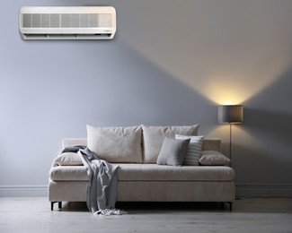 Image of Sofa with pillows, blanket and lamp near grey wall in room. Air conditioner keeping comfortable temperature indoors
