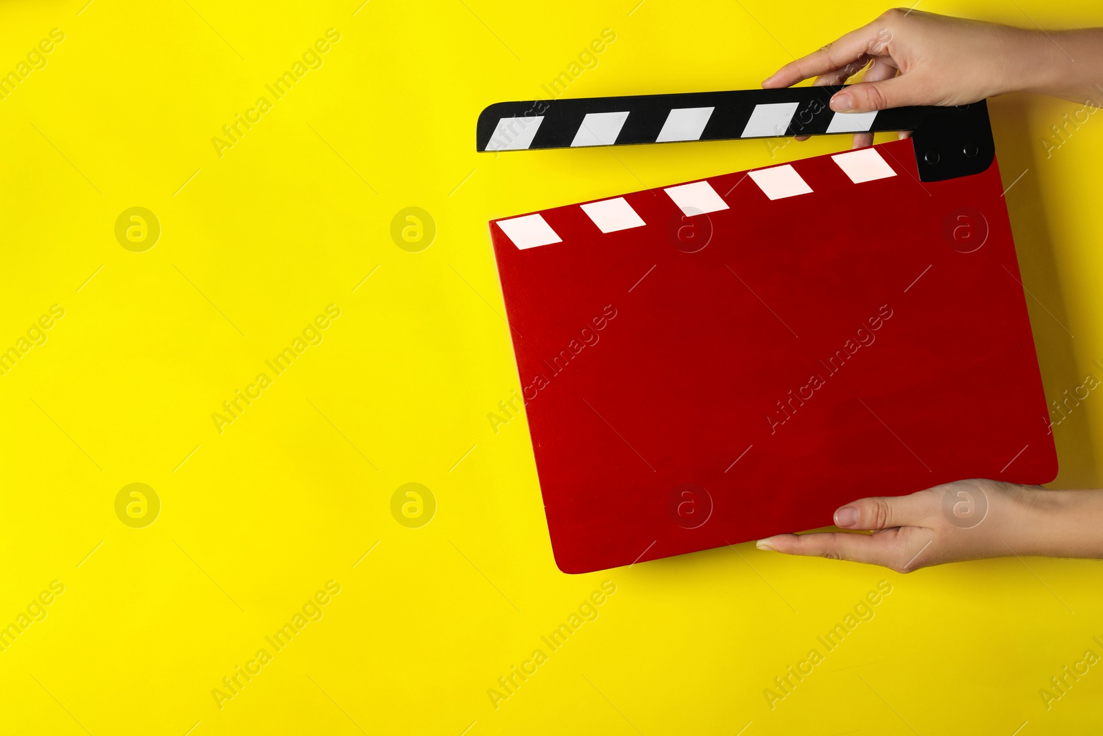 Image of Woman holding red clapperboard on yellow background, closeup with space for text. Film industry