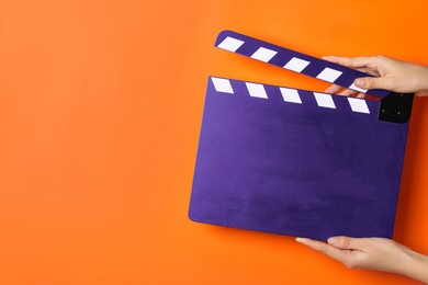 Image of Woman holding purple clapperboard on orange background, closeup with space for text. Film industry