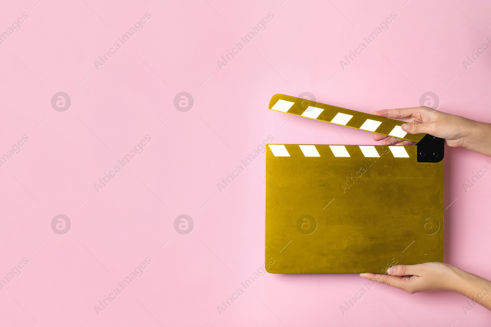 Image of Woman holding golden clapperboard on pink background, closeup with space for text. Film industry