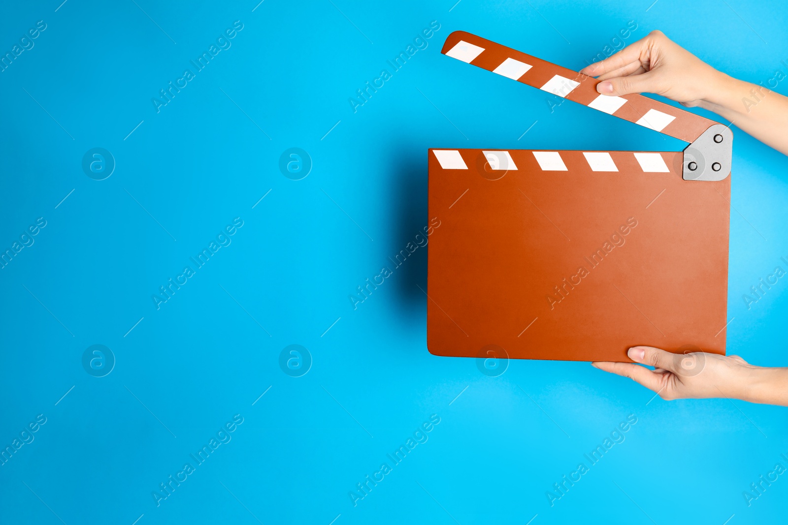 Woman holding orange clapperboard on blue background, closeup with space for text. Film industry Image of Woman holding orange clapperboard on blue background, closeup with space for text. Film industry