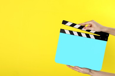 Image of Woman holding cyan clapperboard on yellow background, closeup with space for text. Film industry