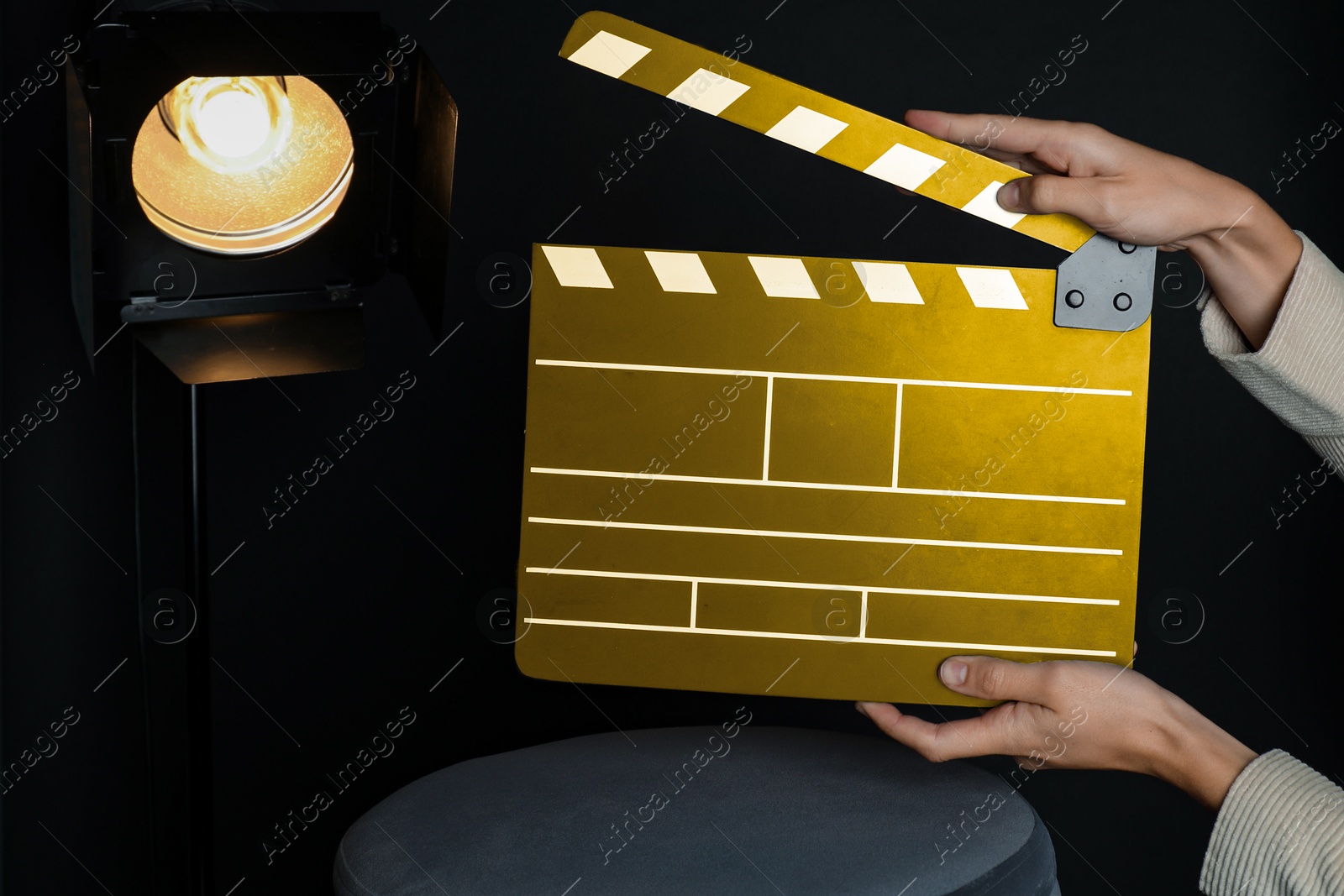 Image of Woman with golden clapperboard near spotlight on black background, closeup