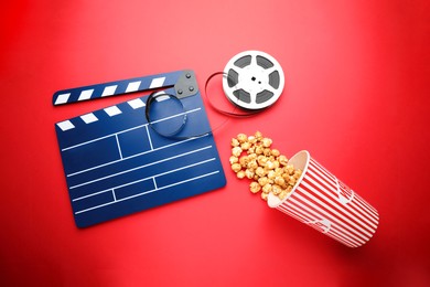 Image of Blue clapperboard, film reel and popcorn on red background, flat lay