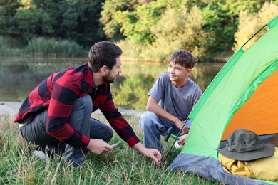Photo of Happy father and son setting up camping tent near river outdoors