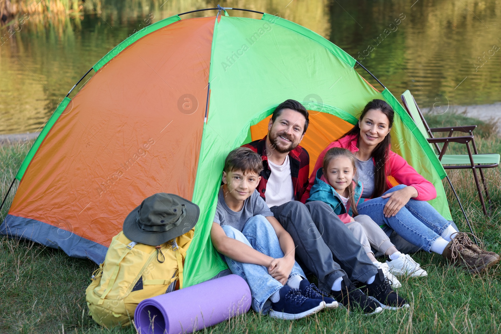 Photo of Happy family spending time together with camping tent and tourist equipment near river outdoors