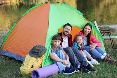 Photo of Happy family spending time together with camping tent and tourist equipment near river outdoors