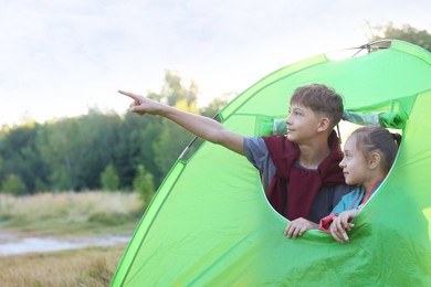 Photo of Brother pointing at something to his sister in camping tent outdoors
