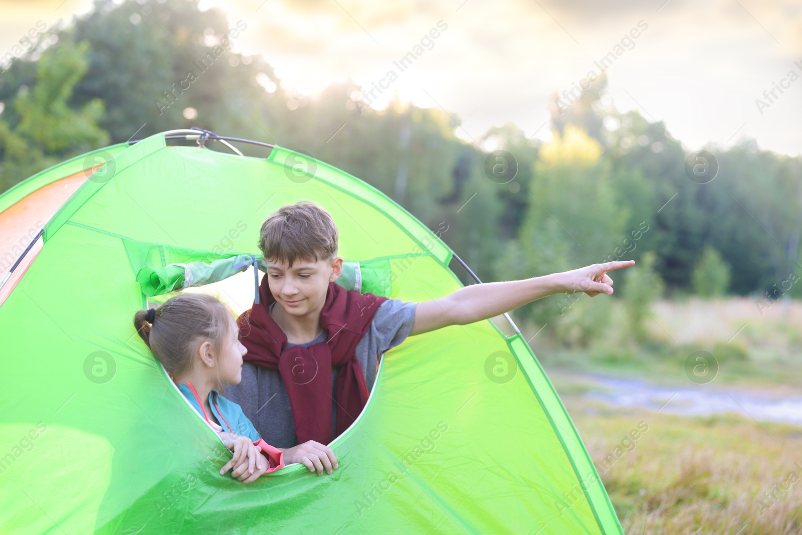 Photo of Brother pointing at something to his sister in camping tent outdoors