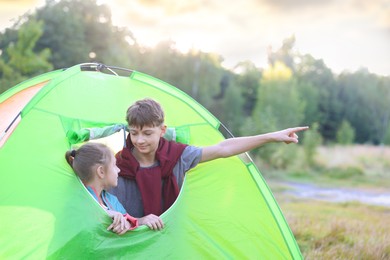 Photo of Brother pointing at something to his sister in camping tent outdoors