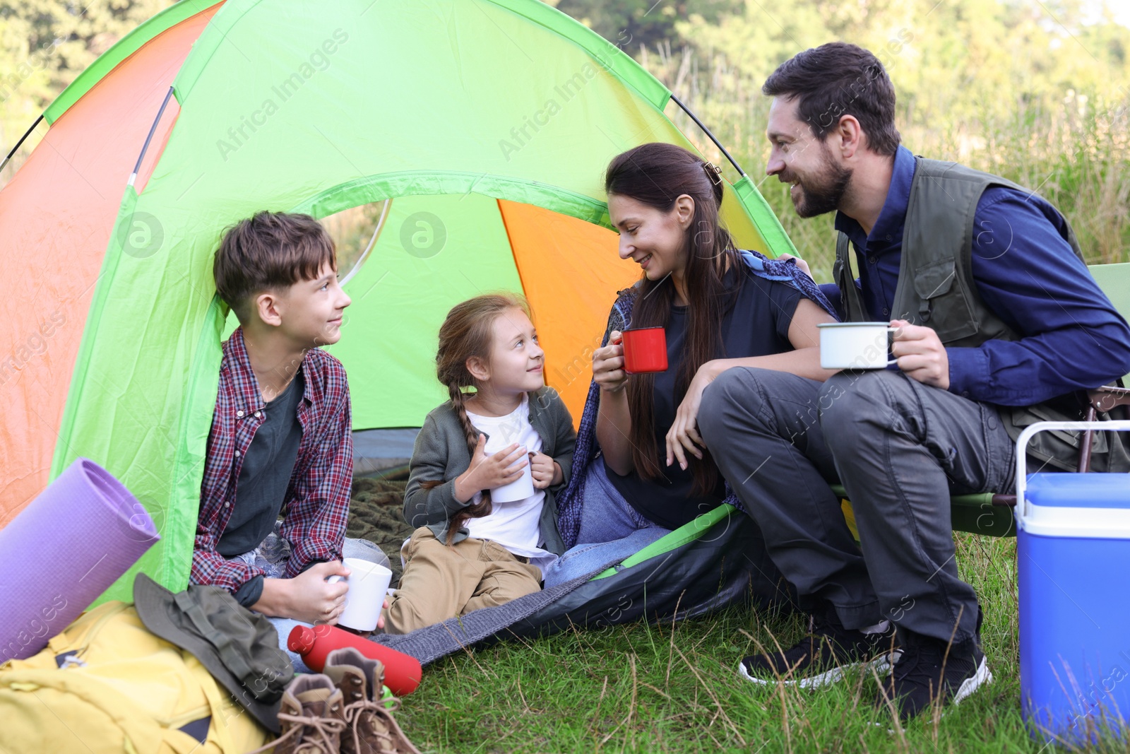 Photo of Happy family spending time together with camping tent, tourist equipment and mugs of hot drink outdoors