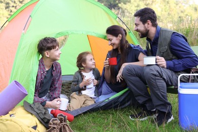 Photo of Happy family spending time together with camping tent, tourist equipment and mugs of hot drink outdoors