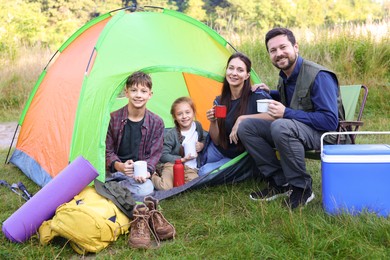 Photo of Happy family spending time together with camping tent, tourist equipment and mugs of hot drink outdoors