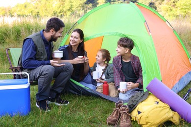 Photo of Happy family spending time together with camping tent, tourist equipment and mugs of hot drink outdoors