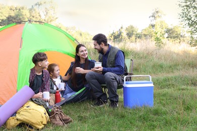 Photo of Happy family spending time together with camping tent, tourist equipment and mugs of hot drink outdoors