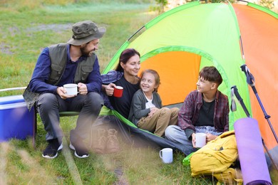 Photo of Happy family spending time together with camping tent, tourist equipment and mugs of hot drink outdoors