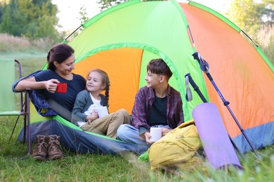 Photo of Family spending time together with camping tent, tourist equipment and mugs of hot drink outdoors